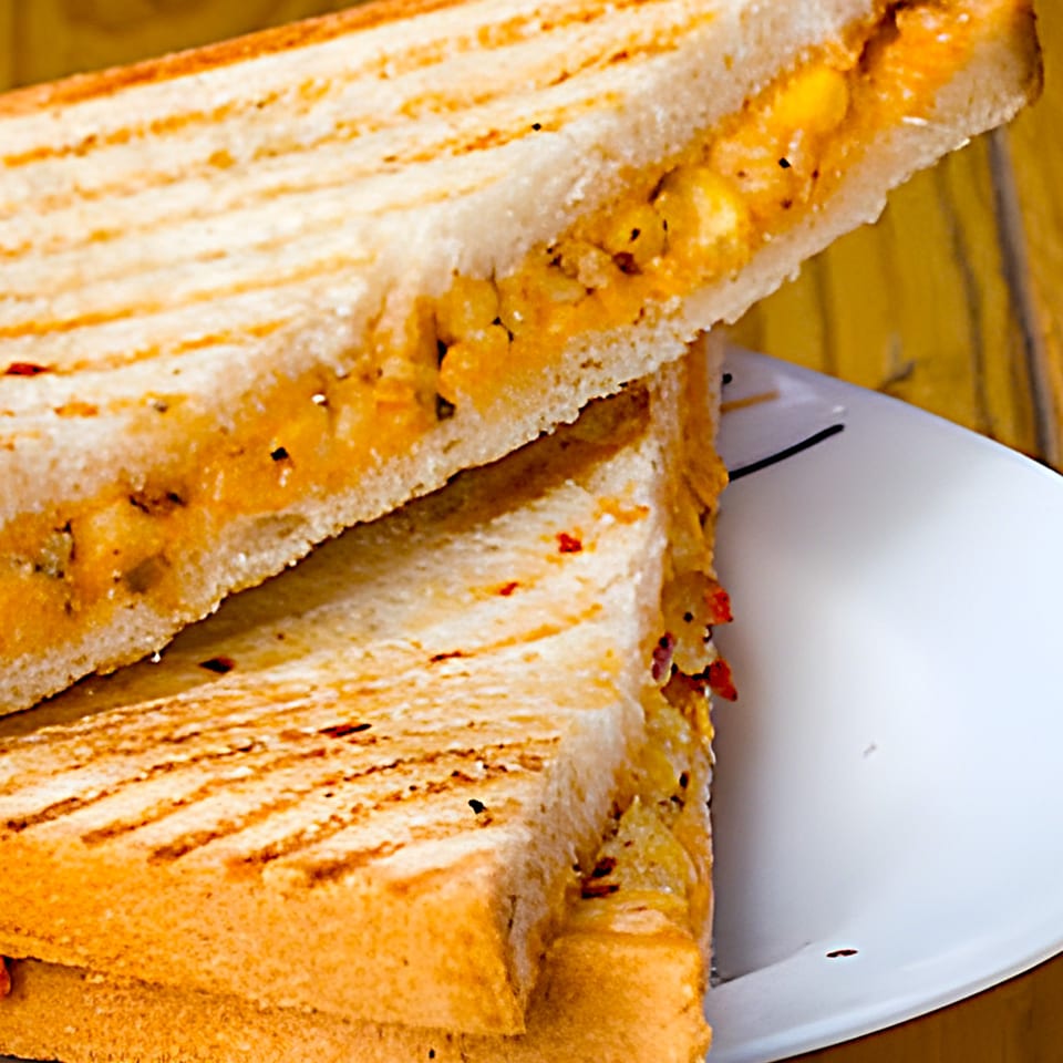 Close-up of a grilled sandwich with a cheesy, corn, and pepper filling on a white plate.